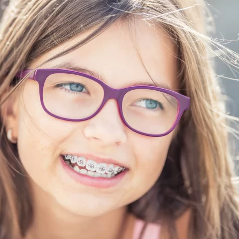 Girl wearing glasses and braces, smiling confidently.